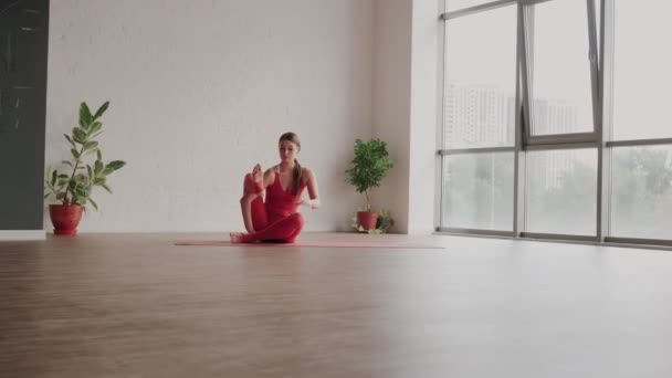 Junge Frau in roter Sportuniform führt Astavakrasana Asana im Yoga-Studio vor. Gleichgewichtsübung — Stockvideo