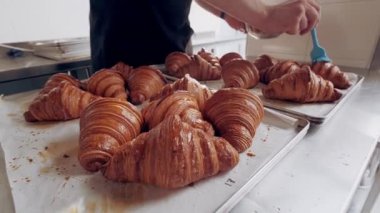Fırıncı fırında taze pişmiş Fransız kruvasanı yağlıyor. Kapat.