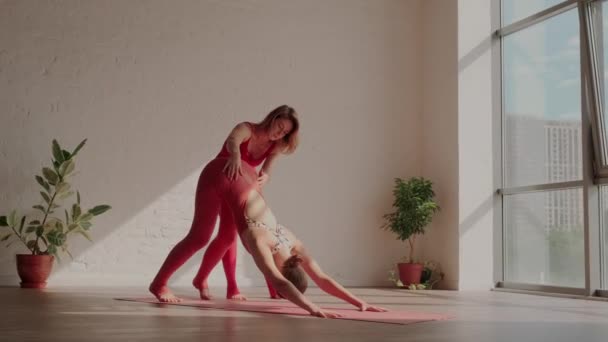 Mujer profesora de yoga ayuda a la estudiante a hacer el Eka Pada Adho Mukha Svanasana correctamente. Errores en el yoga — Vídeos de Stock