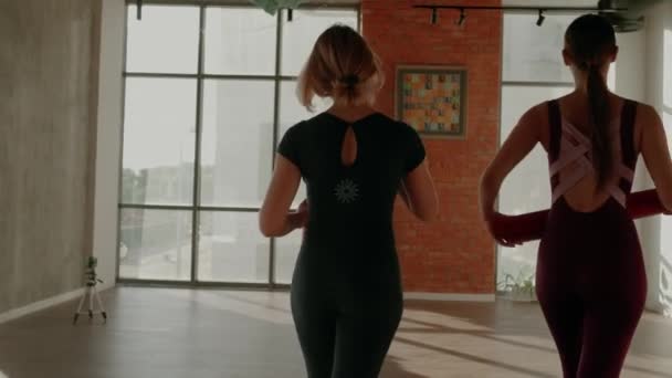 Deux femmes en uniformes de sport entrent dans un studio de yoga, étalent des tapis de yoga et font namaste asana. — Video