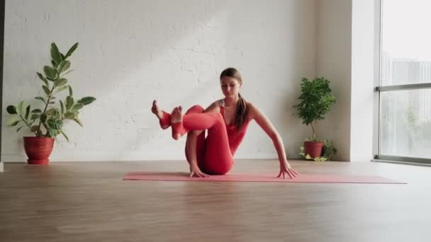Młoda kobieta w czerwonym stroju sportowym wykonuje Astavakrasana asana w studio jogi. Ćwiczenie równowagi — Wideo stockowe