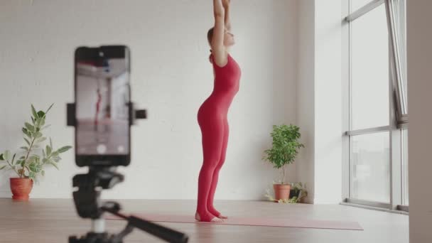 Vrouwelijke yoga leraar registreert online training op haar mobiele telefoon. Home workout yoga concept — Stockvideo
