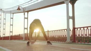 Siyah spor üniformalı genç beyaz adam şafakta yaya köprüsünde koşmadan önce ısınma antrenmanı yapıyor.