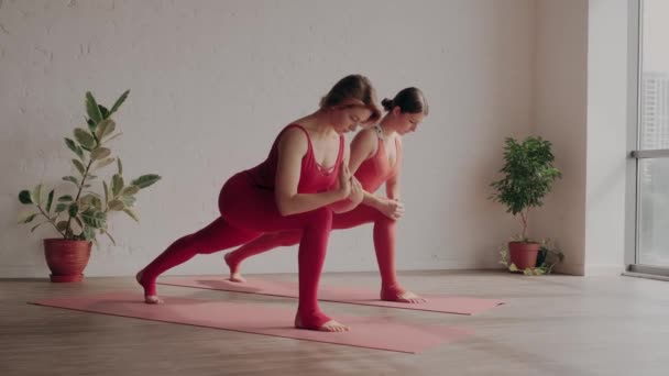 Dwie kobiety w czerwonych strojach sportowych robią virabhadrasana w studiu jogi. Koncepcja zdrowego stylu życia — Wideo stockowe