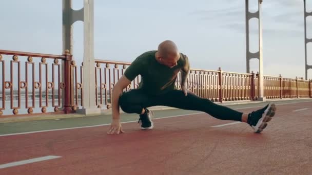 Les hommes européens étirent les jambes sur la passerelle à l'aube avant de faire du jogging. Concept de mode de vie sain — Video