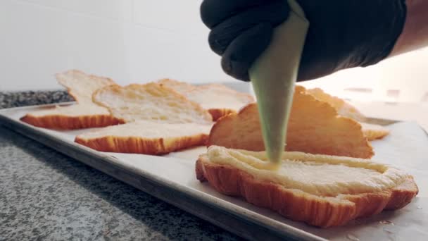 Croissant de almendras. Baker en guantes negros aplica relleno de pasta de almendras al croissant fresco de corte — Vídeo de stock