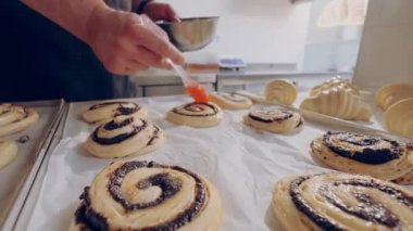 Baker yumurta sarısını çiğ salyangoz çöreğine haşhaş tohumuyla sürer. Pişirme süreci.