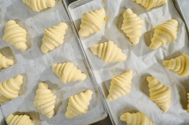 Fırın tepsisinde pişirmeden önce güzel çiğ kruvasanlar. Fırın üretimi. Klasik Fransız hamur işleri.