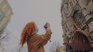 Seyahat et ve ikna ol. Koruyucu maskeli kızıl saçlı kadın arka planda selfie çekiyor..
