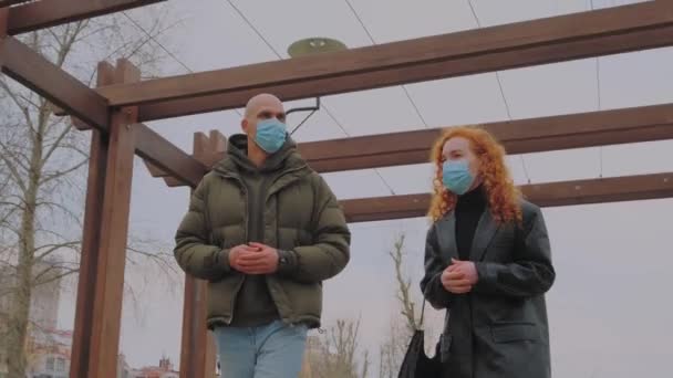 Европейский мужчина и женщина прогуливаются по парку, снимают защитные маски и начинают общаться — стоковое видео
