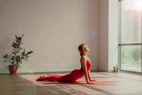 向太阳致敬穿着红色运动服的年轻女子正在瑜伽室做瑜伽 健康的生活方式高质量的照片 图库图片