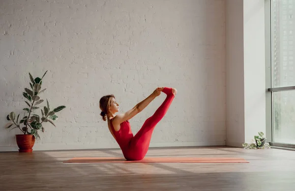 Ubhaya Padangushthasana 穿着红色运动服的年轻女子正在工作室里做瑜伽 健康的生活方式概念 高质量的照片 免版税图库照片