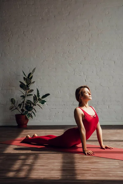 Sun salutation. Young woman in red sports overalls is doing yoga in yoga studio. Healthy lifestyle. High quality photo