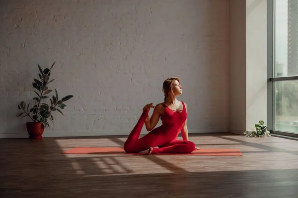 健康的生活方式 身穿红色运动服的年轻女子在轻便瑜伽演播室里伸展腿 拖延时间 高质量的照片 图库图片
