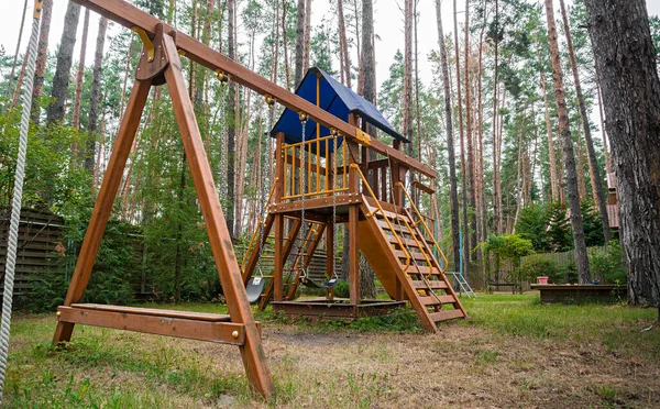 Childrens wooden playground recreation area at forest. Wooden house with gazebo, lawn and concrete walkway in the forest. High quality photo