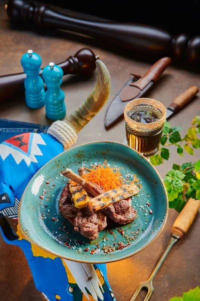 Fried juicy steak. Lamb rack on a blue plate on a beautiful rusty background with a skeleton of a cows head. Argentine cuisine. High quality photo