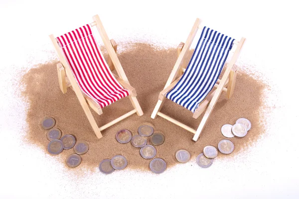 Монеты номиналом 1 и 2 евро лежат перед игрушечными пляжными стульями — стоковое фото