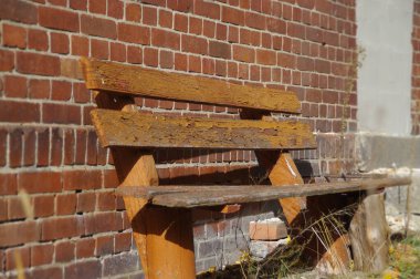 Arka planda tuğla duvar olan eski kahverengi bank. Dinlenmek için harika bir yer. Boş ahşap ve yıpranmış koltuk unutulmuş dış yüzeyde..