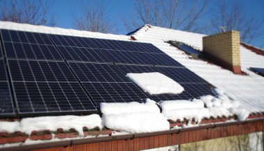 Güneş panelleri karla kaplı. Güneşli bir günde kış mevsiminde evin çatısına fotovoltaik elektrik kurulumu. Soğuk havada alternatif enerji üretimi.