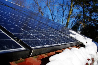 Kar ve buzla kaplı güneş panelleri. Evin çatısında fotovoltaik elektrik tesisatı var. Güneşli bir günde kış mevsimi. Düşük performans ve verimlilikle alternatif PV enerji üretimi.