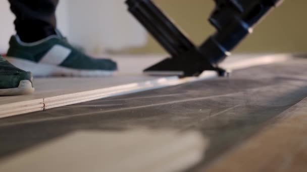Menutup gambar Man memasang ubin lantai parket di atas lapisan dasar busa putih, memalu paku dengan palu mekanis khusus — Stok Video