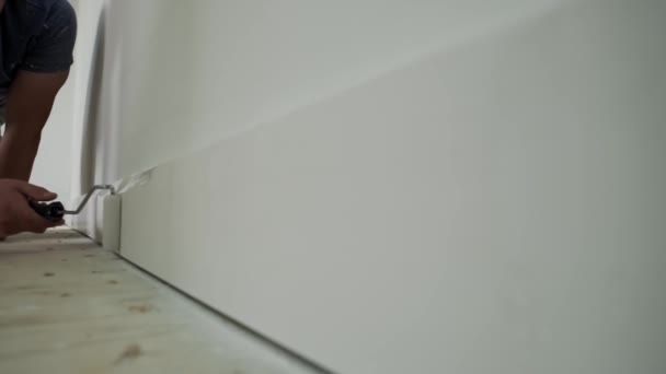 Pintor pintando el borde de la pared con rodillo. Práctico cuadro sobre molduras, zócalo. Movimiento lento — Vídeos de Stock