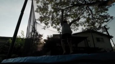 Yazın arka bahçede trambolinde hoplayıp zıplayan çocuk.