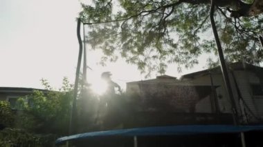 Yazın arka bahçede trambolinde hoplayıp zıplayan çocuk. Yavaş çekim.