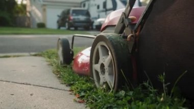 Çocuk parkındaki salıncağın yanında çim biçme makinesiyle çim biçen bir adam var. Yavaş çekim görünümü