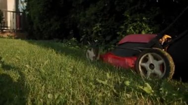 Çocuk parkındaki salıncağın yanında çim biçme makinesiyle çim biçen bir adam var. Yavaş çekim gelecek.