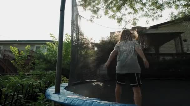 Мальчик прыгает на батуте на заднем дворе летом. Вид на медленное движение — стоковое видео