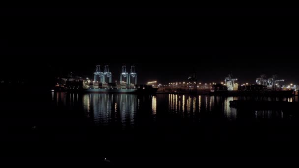 貨物コンテナを搭載した貨物船の広い空中表示は、夜間のコンテナの積み降ろし時に港内のバースに立つ — ストック動画
