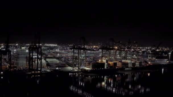 Szeroki widok z powietrza. Statek towarowy z kontenerami ładunkowymi stoi na koi w porcie przy załadunku i rozładunku kontenerów w nocy.. — Wideo stockowe