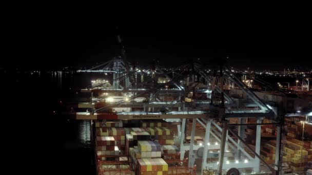 Drohne weite Sicht auf Frachtschiff mit Frachtcontainern steht auf einem Liegeplatz im Hafen beim Be- und Entladen von Containern in der Nacht.. — Stockvideo