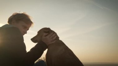 Gün batımında bir köpekle oturan kadın siluetleri.