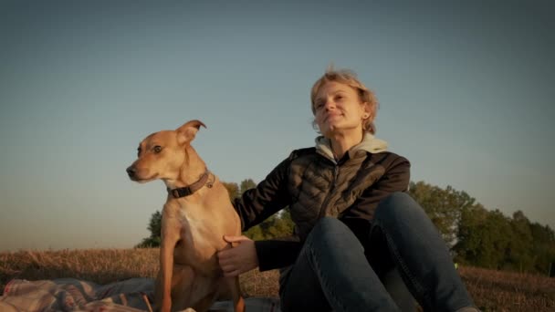 Vrouw zittend met een hond tijdens zonsondergang — Stockvideo