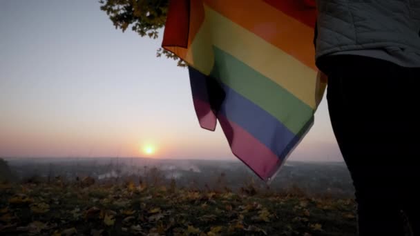 Woman waving rainbow LGBT flag on sunset. Slow motion