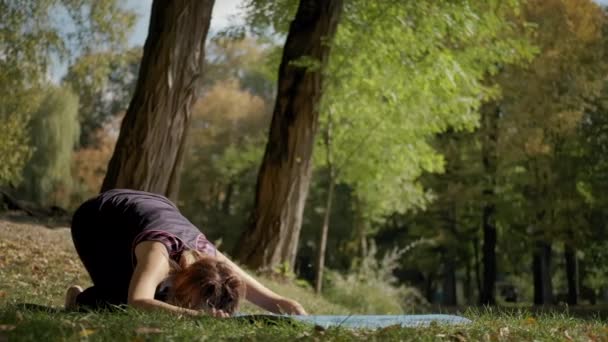 Nő ül a jóga szőnyegen és gyakorolja jóga nyújtás gyakorlat a szabadban a napsütéses napon. — Stock videók