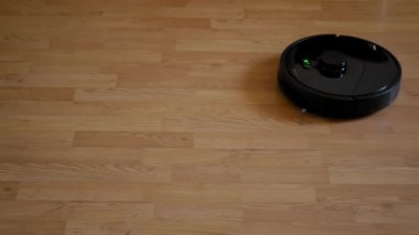 Üst görüntü. Akıllı elektrikli süpürge robotu oturma odasında ahşap zeminde koşar.