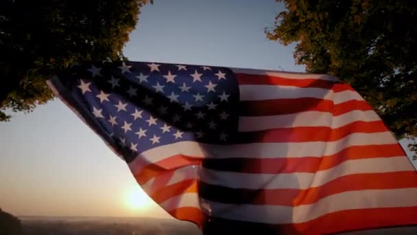 Visão traseira da mulher feliz com a bandeira nacional dos EUA em pé ao ar livre ao pôr do sol. Fechar — Vídeo de Stock