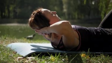 Yakın çekim. Yoga minderinde oturan ve güneşli bir günde dışarıda yoga esneme egzersizi yapan bir kadın. Geniş açı