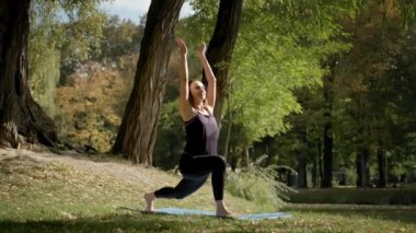 Yoga minderinde oturan ve açık havada yoga esneme egzersizi yapan bir kadın. Yavaş çekim
