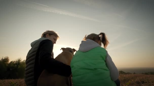 Siluetas de mujer con hija pequeña y perro mascota sentado durante la puesta del sol increíble. Amplio tiro — Vídeos de Stock