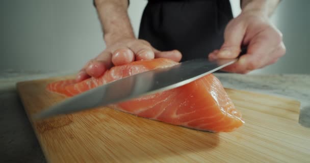 Vista de cerca de la mano del chef masculino profesional utilizando cuchillo rebanada de carne de salmón de naranja fresca en la tabla de cortar en la cocina del restaurante. — Vídeo de stock