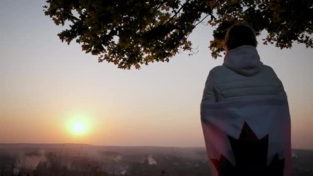 日落时，一个女人站在晴朗的天空中，拿着加拿大的国旗. — 图库视频影像