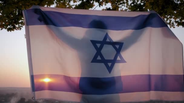 Een vrouw staat met de vlag van Israël tegen een heldere lucht bij zonsondergang. — Stockvideo