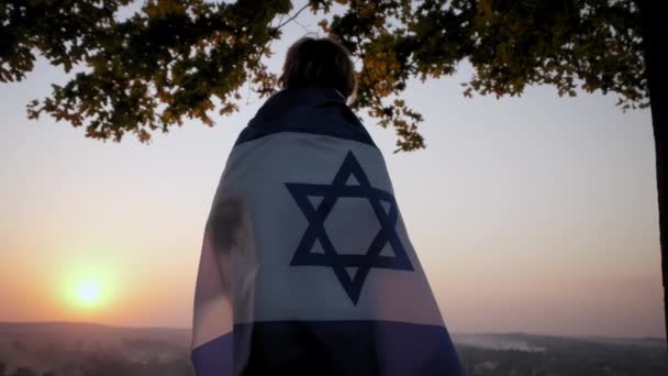 Een vrouw staat met de vlag van Israël tegen een heldere lucht bij zonsondergang. Close-up beelden — Stockvideo