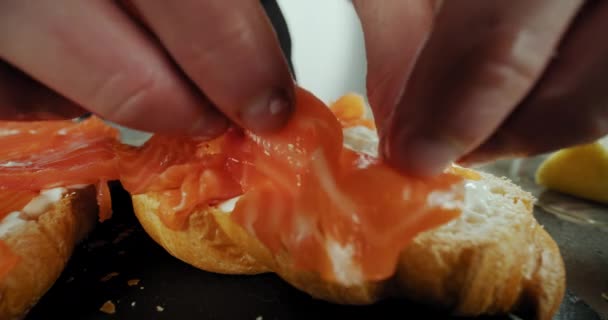 El chef cocina sándwich de croissant con queso crema, salmón y huevo en un plato negro — Vídeos de Stock