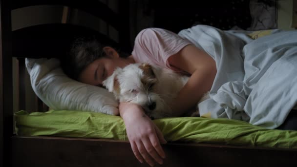 Uma adolescente dorme com o cão Jack Russell Terrier na cama. .. amizade das crianças e seus animais de estimação. Vista ampla — Vídeo de Stock