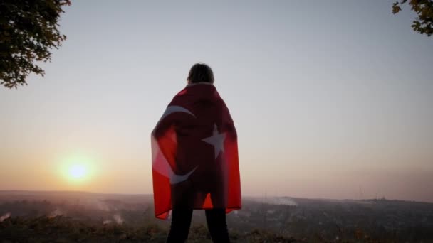 夕暮れ時に屋外に立ってトルコ国旗を持つ幸せな女性のバックビュー。スローモーションが始まった — ストック動画